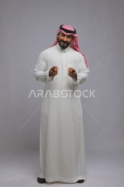Expressions of certainty and astonishment, pointing to something with astonished gestures, portrait of a Saudi Gulf Arab man wearing the traditional dress and shemagh, raising his fingers to identify and choose, full-length portrait, gray background