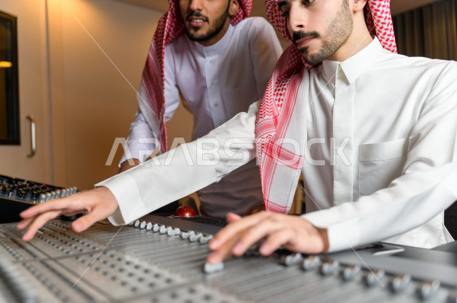 شابان سعوديان في غرفة خارج الاستديو ،يتم معالجةالاصوات المسجلة داخل الاستديو عن طريق برمجيات صوتية من خلال جهاز الحاسوب المخصص ، استديو تسجيل صوتي ، بث مباشر ، فريق الاعداد ، الاذاعة الصوتية ، نشرات اخبارية