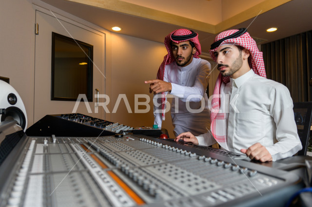 شابان سعوديان في غرفة خارج الاستديو ،يتم معالجةالاصوات المسجلة داخل الاستديو عن طريق برمجيات صوتية من خلال جهاز الحاسوب المخصص ، استديو تسجيل صوتي ، بث مباشر ، فريق الاعداد ، الاذاعة الصوتية ، نشرات اخبارية
