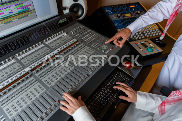 شابان سعوديان في غرفة خارج الاستديو ،يتم معالجةالاصوات المسجلة داخل الاستديو عن طريق برمجيات صوتية من خلال جهاز الحاسوب المخصص ، استديو تسجيل صوتي ، بث مباشر ، فريق الاعداد ، الاذاعة الصوتية ، نشرات اخبارية