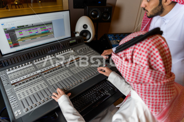 شابان سعوديان في غرفة خارج الاستديو ،يتم معالجةالاصوات المسجلة داخل الاستديو عن طريق برمجيات صوتية من خلال جهاز الحاسوب المخصص ، استديو تسجيل صوتي ، بث مباشر ، فريق الاعداد ، الاذاعة الصوتية ، نشرات اخبارية