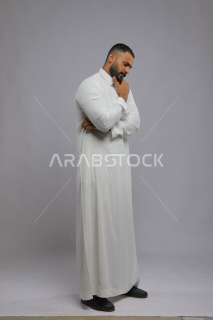 Gestures of contemplation and concentration, thinking and contemplation, absent-mindedness and planning for the future, portrait of a Saudi Gulf Arab young man wearing a traditional dress, finding a solution to a problem, full-length body portrait, gray background