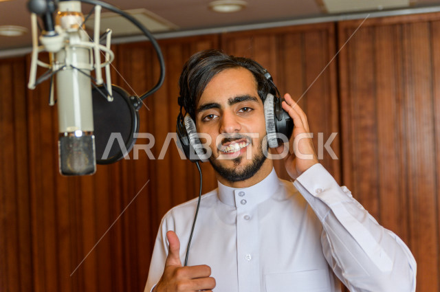 مذيع سعودي داخل الاستديو ، تسجيل الصوت من خلال المايكروفون ،  استديو تسجيل صوتي ، بث مباشر ، فريق الاعداد ، الاذاعة الصوتية ، نشرات اخبارية