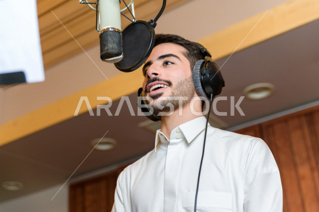 مذيع سعودي داخل الاستديو ، تسجيل الصوت من خلال المايكروفون ،  استديو تسجيل صوتي ، بث مباشر ، فريق الاعداد ، الاذاعة الصوتية ، نشرات اخبارية