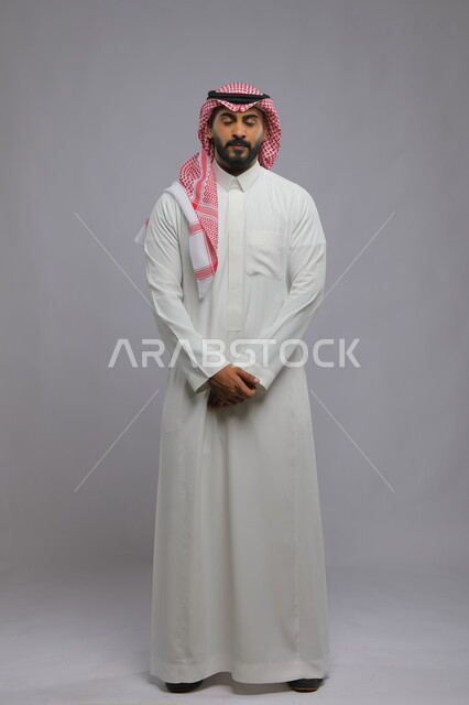 مفهوم الاسترخاء والراحة, الشعور بالنعاس و الرغبه في النوم ، بورتريه لشاب عربي خليجي سعودي يرتدي الشماغ والثوب التقليدي يقف باستقامة مغمض العينين، التأمل وشرود الذهن، صورة الجسم بالكامل، خلفية رمادية