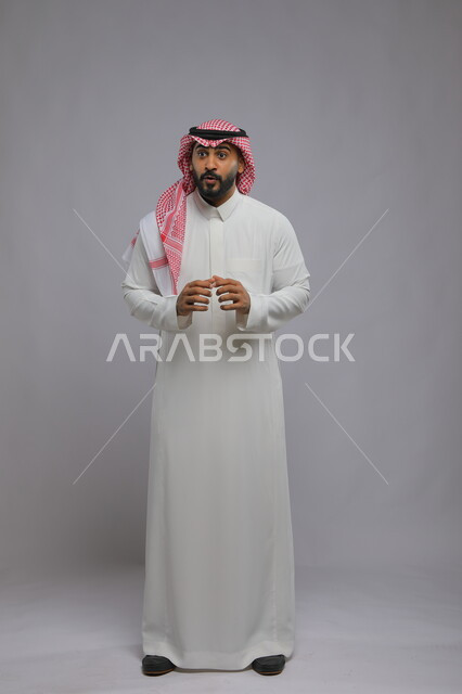 ايماءات الذعر و القلق والدهشة والتعجب، بورتريه لرجل عربي خليجي سعودي يرتدي الثوب التقليدي والشماغ يقف باستقامة وينظر لمكان معين بتعابير الارتباك، المفاجأة في رؤية شيء ما، صورة الجسم بالطول الكامل، خلفية رمادية
