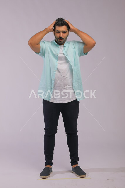 الشعور بالعجز وعدم المعرفة، بورتريه لشاب عربي خليجي سعودي يرتدي اللباس الكاجوال يرفع يديه على رأسه, التفكير في إيجاد حل لمشكلة ما, صورة الجسم بالطول الكامل, خلفية رمادية.