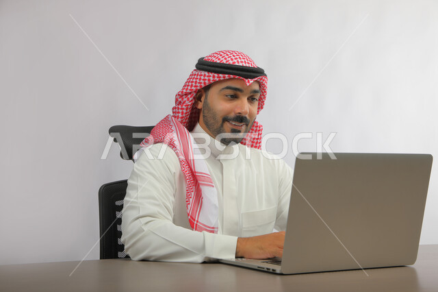 عقد اجتماع عمل عن بعد، استخدام التقنيات الحديثة المتطورة, بورتريه لرجل عربي خليجي سعودي يرتدي الزي التقليدي يجلس أمام جهاز الحاسوب، الدردشة مع الأهل والأصدقاء, متابعه آخر أخبار السوشال ميديا، تطبيقات وبرامج الأجهزة اللوحية، خلفية رمادية.