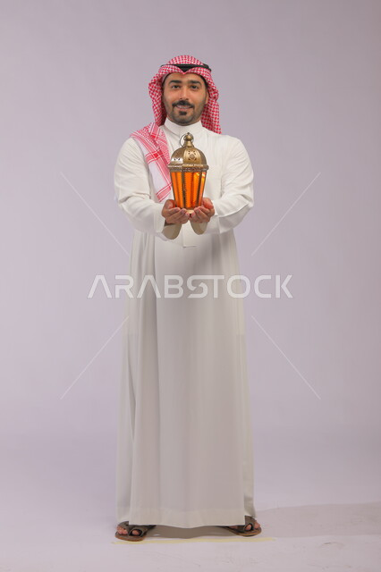 المناسبات الدينية والأعياد الإسلامية, الاستعداد لقدوم شهر رمضان, بورتريه لشاب عربي خليجي سعودي مبتسم يرتدي الثوب التقليدي والشماغ يحمل الفانوس المضيء, تحف وزينة الاحتفالات في السعودية, صورة الجسم بالكامل, اسلاميات وعبادة, خلفية رمادية