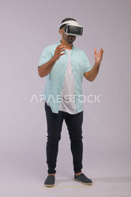 Conducting interactive experiences through virtual reality glasses, a portrait of a Saudi Gulf Arab man wearing casual summer clothes and wearing 3D glasses, using modern technology and technique, full-length body portrait, white background.