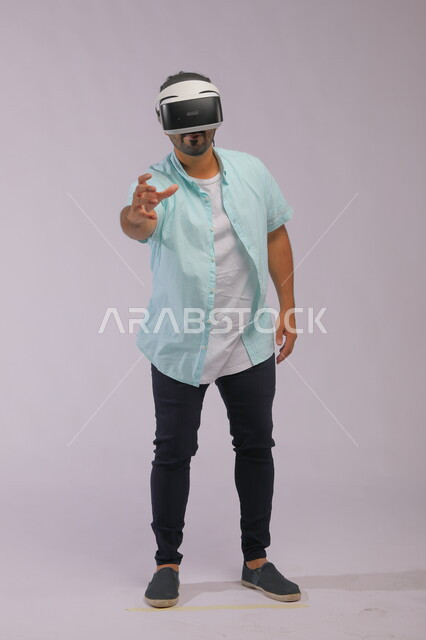 تجربة واقعية باستخدام نظارات الواقع الافتراضي، بورتريه لرجل عربي سعودي خليجي يرتدي ملابس كاجوال صيفية ويضع النظارات ثلاثية الابعاد، تحسين التواصل بين الأفراد من خلال التقنية الحديثة، صورة لكامل الجسم، خلفية بيضاء