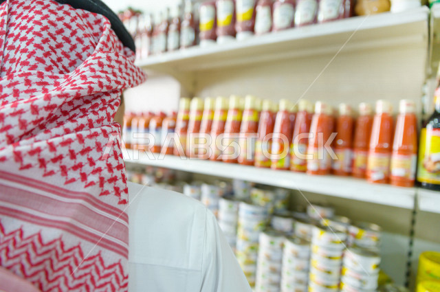 رجل سعودي خليجي يتبضع في قسم المعلبات الغذائية داخل السوبرماركت ، شراء الاحتياجات المنزلية ، السلع والمواد غذائية المختلفة ، مستلزمات المستهلك