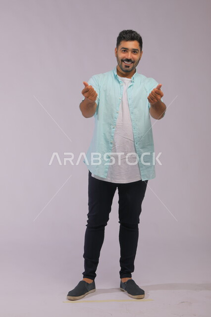  الإشارة بإيماءات طلب الصبر والتأني والتريث، بورتريه لرجل عربي خليجي سعودي يرتدي الزي الكاجوال يقف لطلب الأموال الكثيرة, السرور بالصفقات الناجحة والنمو الاقتصادي والمالي, صورة الجسم بالطول الكامل, خلفية رمادية.