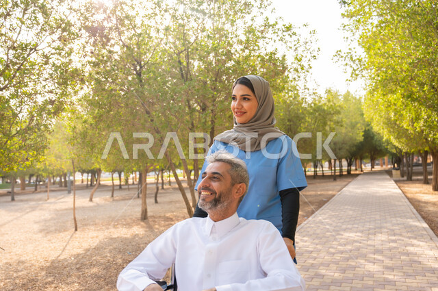 قوة العزيمة والتحدي عند أصحاب الهمم, صورة مقربة لرجل كبير السن عربي خليجي سعودي مبتسم مقعد يرتدي الثوب التقليدي يجلس على كرسي متحرك برفقة ممرضته الخاصة في إحدى الحدائق العامة، نزهه في الطبيعه والهواء الطلق، شعور المعاقين بالإنتماء والتقدير والإحترام في السعوديه