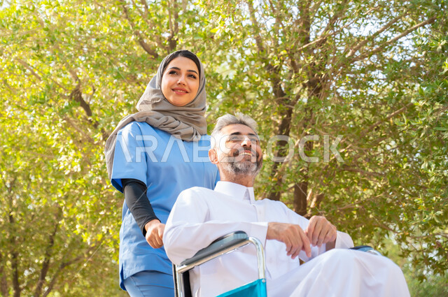 التحسين من نفسية المرضى بالتنزه في الهواء الطلق، قوة العزيمة والتحدي عند أصحاب الهمم, رجل كبير السن عربي خليجي سعودي مبتسم مقعد يرتدي الثوب التقليدي يجلس على كرسي متحرك برفقة ممرضته الخاصة في إحدى الحدائق العامة، شعور المعاقين بالإنتماء والتقدير في السعوديه