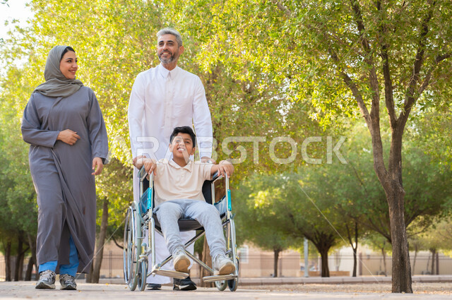 أجواء عائلية مليئة بالحب، الاعتناء بالأبناء المعاقين والتحسين من نفسيتهم، عائلة عربيه خليجيه سعودية تقوم بالتنزه في إحدى الحدائق العامة ،ولد سعودي من ذوي الهمم يجلس على كرسي متحرك برفقة والديه في الخارج للاستمتاع بأوقات الفراغ، الحنان والعطف بين أفراد الأسرة