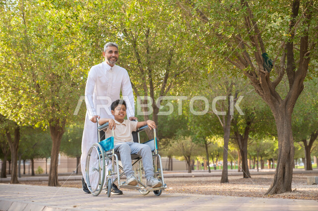 الاستمتاع بالأجواء الصيفيه ،أدوات تساعد مرضى ذوي الإعاقة الحركية على التنقل بسهولة, تحسين حياة أصحاب الهمم وتأمين احتياجاتهم الخاصة, رجل مسن عربي خليجي سعودي يرتدي الزي التقليدي برفقة ابنه في إحدى الحدائق، ولد سعودي مقعد يجلس على كرسي متحرك في الخارج