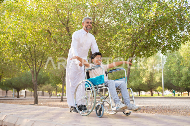 Tools that help patients with mobility disabilities move easily, improve the lives of people of determination and provide for their special needs, an elderly Saudi Arabian Gulf man wearing traditional clothing with his son in a park enjoying the outdoors, a disabled Saudi boy sitting in a wheelchair extending his hands to the side