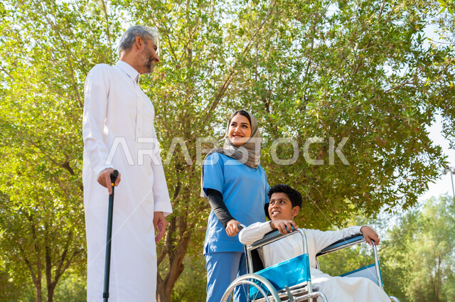مفهوم الرعاية الصحية والاعتناء بالمرضى والمعاقين, رجل كبير السن عربي خليجي سعودي يرتدي الزي التقليدي يستخدم العكاز للمساعدة على السير مع ابنه، ممرضة تهتم بولد من ذوي الاحتياجات الخاصة, تبادل الحديث بإيماءات السعادة, المشي في الحدائق العامة تحت ضوء الشمس.