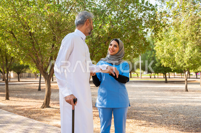 ممرضة تقوم بمساعدة مريضها للتنزه في الحديقة واستنشاق الهواء الطلق، إيماءات البشاشة والمعاملة الحسنة ، رجل شايب عربي خليجي سعودي يرتدي الزي التقليدي يستخدم العكاز للمساعدة على المشي، مفهوم الخدمات والعناية الطبية, شحن الهمم بالطاقة الإيجابية.