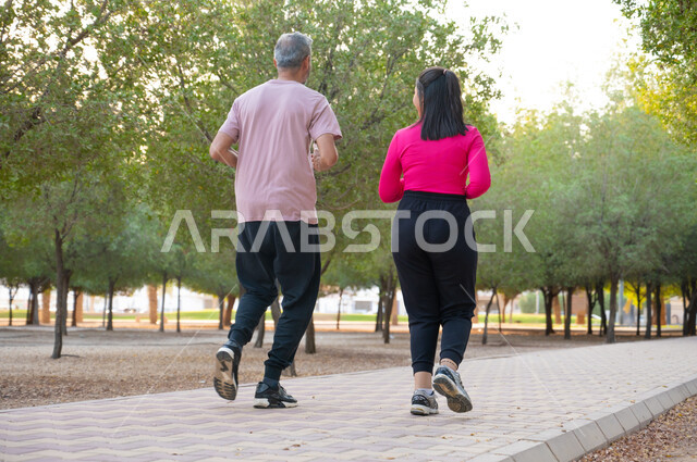 نمط الحياة الصحية، تبادل الأحاديث المسلية أثناء القيام بالتمارين الرياضية ،الحفاظ على اللياقة والرشاقة البدنية، صورة من الخلف لصديقان عربيان خليجيان سعوديان يرتديان الزي الرياضي ويقومان بممارسة الرياضة الصباحية في أحد الحدائق ، قضاء أوقات ممتعة مع الأخوة