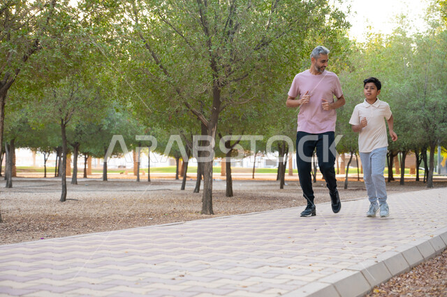قضاء أوقات ممتعه في الخارج مع الأولاد ،رجل وولده عربيان خليجيان سعوديان يرتديان الملابس الرياضية ويقومان بممارسة التمارين الصباحية في أحد ممرات الحدائق العامة، الحفاظ على الصحة الجسدية، تربيه الابناء على مفهوم الاهتمام باللياقة البدنية