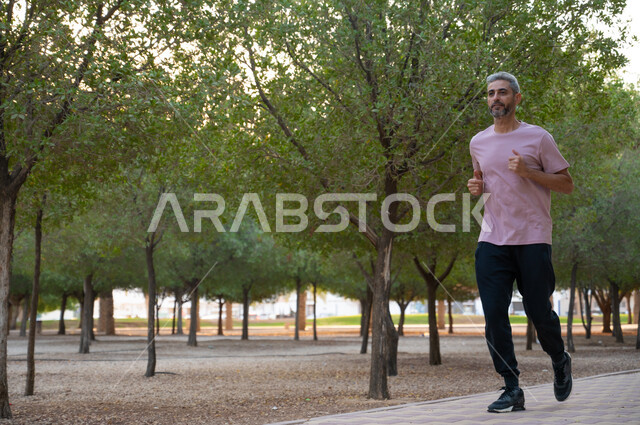 ممارسة رياضة المشي في أحد الحدائق العامة ،الرشاقه والصحة البدنية, رجل كبير السن عربي خليجي سعودي يرتدي الملابس الرياضية و يقوم في ممارسة التمارين الصباحية في الهواء الطلق، المحافظة على اللياقة الجسدية، أنشطة ورياضات ترفيهية