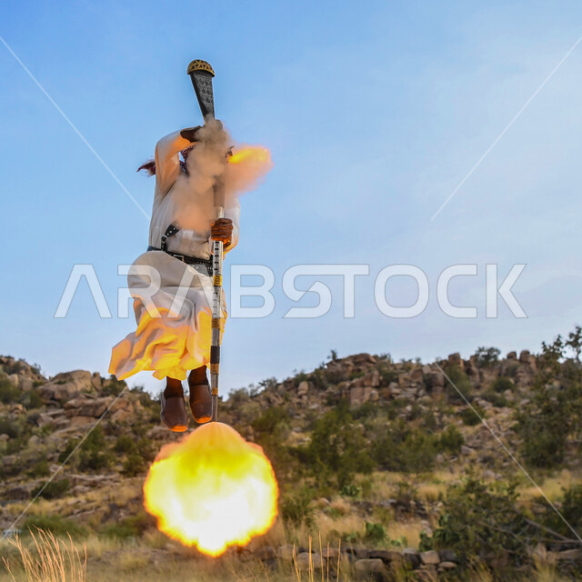 بث الثقة والحماس قبل خوض المعركة، رجل عربي خليجي سعودي من العرضة الحجازية يرتدي الملابس الشعبيه يؤدي الرقص الحربي القديم يالمقمع ، فن التعشير و عروض الفلكلور التراثي ، التعبير عن الفرح بالانتصار ،خلفية الطبيعه