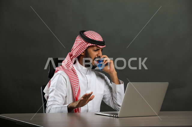 الصراخ والتوتر والضغط، الاستفسار والسؤال عن شيء ما، إيماءات اللوم والتأنيب والانزعاج، بورتريه لرجل أعمال عربي  سعودي خليجي يرتدي الشماغ والثوب التقليدي يجري مكالمة هاتفيه باستخدام الهاتف المحمول، عدم الالتزام بالمخططات والاتفاقيات ، خلفية رمادية .