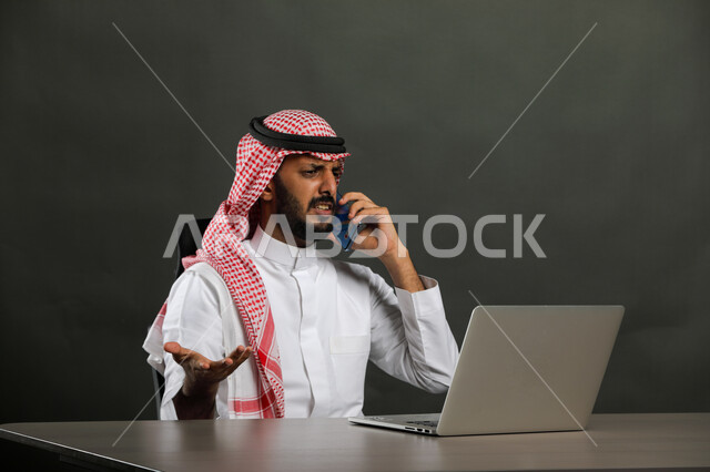 الاستفسار والسؤال عن شيء ما، إيماءات اللوم والتأنيب والانزعاج، بورتريه لرجل أعمال عربي  سعودي خليجي يرتدي الشماغ والثوب التقليدي يجري مكالمة هاتفيه باستخدام الهاتف المحمول، عدم الالتزام بالمخططات والاتفاقيات ، التهيج والتوتر والضغط، خلفية رمادية .