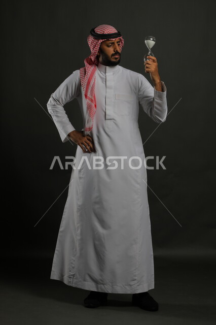 الاهتمام بنباتات الزينة, العناية بالشتلات المنزلية, بورتريه لرجل عربي خليجي سعودي يرتدي الثوب التقليدي والشماغ ييتأمل حوض زراعي صغير, الوقوف باستقامة والنظر إلى الكاميرا بإيماءات الاندماج والتفكير, صورة الجسم بالطول الكامل, خلفية رمادية