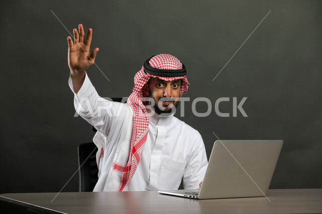 الشعور بالرفض وطلب عدم التدخل, ايماءات المنع والتوقف عن فعل شيء ما, بورتريه مقرب لرجل عربي خليجي سعودي يرتدي الثوب التقليدي والشماغ يرفع يديه للأعلى,  الجلوس أمام جهاز الحاسوب وإدارة الأعمال المكتبية, خلفية رمادية
