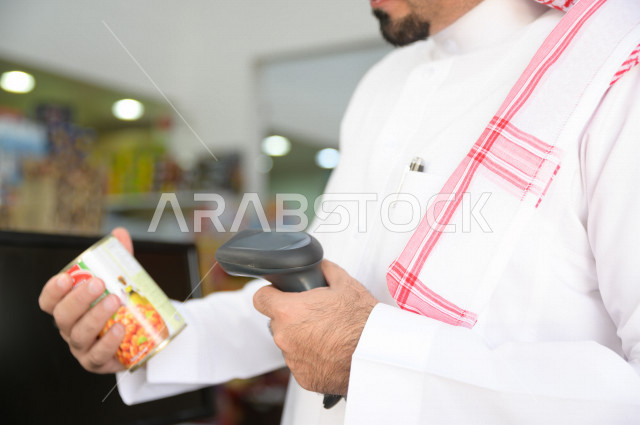 رجل سعودي خليجي يقوم بتسعير احتياجاته الشرائية عند المحاسب  ، شراء الاحتياجات المنزلية داخل السوبرماركت ، السلع والمواد غذائية المختلفة ، مستلزمات المستهلك
