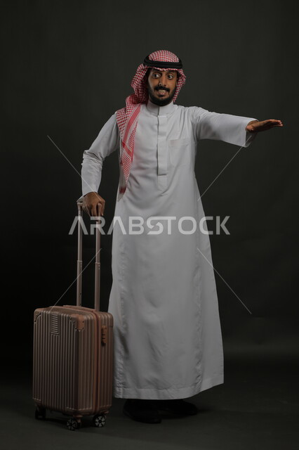 Passenger delivery and transportation service, waiting for the car to arrive, portrait of a Saudi Gulf Arab man wearing the traditional dress and shemagh, holding a suitcase and raising his hands to indicate a car, full-length body portrait, gray background