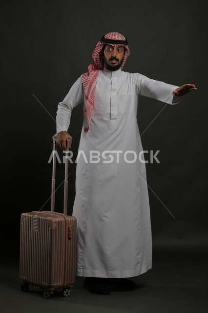 Passenger delivery and transportation service, waiting for the car to arrive, portrait of a Saudi Gulf Arab man wearing the traditional dress and shemagh, holding a suitcase and raising his hands to indicate a car, full-length body portrait, gray background