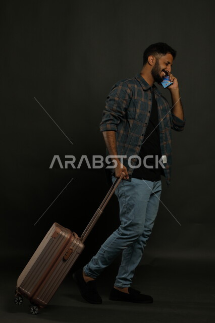 إجراء مكالمة هاتفية عبر الجوال بتعابير السرور، التحدث مع الأهل والأقارب قبل مغادرة البلاد، بورتريه لشاب عربي خليجي سعودي يرتدي الزي الكاجوال يقوم بجر حقيبة السفر خلفه ،ايماءات المشي والذهاب إلى المطار، صورة الجسم بالطول الكامل، خلفية سوداء