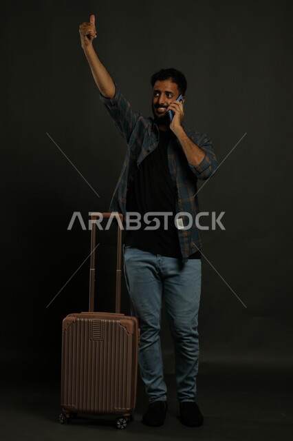 طلب التواصل عبر الهاتف المحمول, محادثات ودردشات و صداقات , بورتريه لشاب عربي سعودي خليجي مبتسم يرتدي الزي الكاجوال ينظر إلى شيء ما، اشارات تدل على الاخبار بإجراء مكالمة هاتفيه عبر الجوال، مفهوم السفر والسياحة، صورة الجسم بالطول الكامل، خلفية سوداء