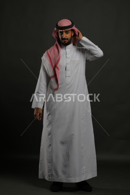 الثقة بالنفس والشعور بالقوة، الاهتمام بالمظهر الخارجي، بورتريه لرجل عربي خليجي سعودي يرتدي الزي التقليدي والشماغ وينظر إلى الكاميرا بجدية، مفهوم الاناقه والرجولة، صورة لكامل الجسم، الوقوف باستقامة وانضباط، خلفية رمادية