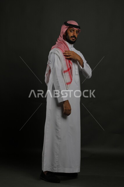 الوقوف باستقامة وثقه بالنفس،  الاهتمام بالمظهر الخارجي، بورتريه لرجل عربي خليجي سعودي يرتدي الزي التقليدي والشماغ وينظر إلى الكاميرا بجدية، مفهوم الاناقه والرجولة، صورة الجسم بالطول الكامل، خلفية رمادية