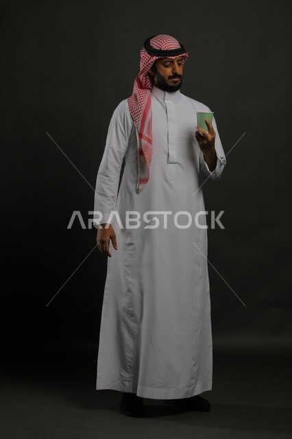 احتساء المشروبات الساخنه, الاستمتاع بمذاق القهوة العربية، بورتريه لرجل عربي خليجي سعودي يرتدي الزي السعودي التقليدي يحمل بيده كوب من الورق المقوى, صورة الجسم بالطول الكامل، خلفية سوداء