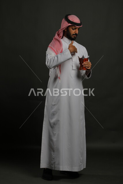 استخدام خشب العود بالأعياد والمناسبات, التطيب بالعطور والبخور, بورتريه لشاب عربي خليجي سعودي يرتدي الشماغ والثوب التقليدي ويحمل المبخرة, الأناقة والاهتمام بالمظهر الخارجي, العادات والتقاليد السعودية, صورة الجسم بالطول الكامل, خلفية رمادية