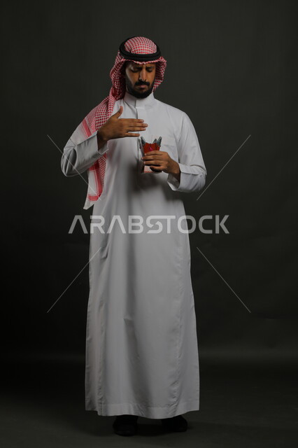 التطيب بالعطور والبخور, استخدام خشب العود بالأعياد والمناسبات, بورتريه لرجل عربي خليجي سعودي يرتدي الشماغ والثوب التقليدي ويحمل المبخرة, الأناقة والاهتمام بالمظهر الخارجي, العادات والتقاليد السعودية, صورة الجسم بالطول الكامل, خلفية رمادية