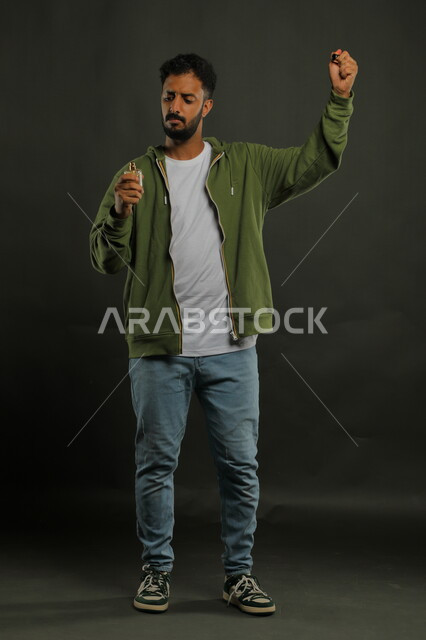 عطورات خليجية سعودية, التسويق لمنتجات العطور, مفهوم التعطر والتطيب, الاهتمام بالمظهر الخارجي, استخدام الزيوت العطرية الطبيعية, بورتريه لشاب عربي خليجي سعودي يرتدي الزي الكاجوال يقوم برش العطر, صورة الجسم بالطول الكامل, خلفية سوداء