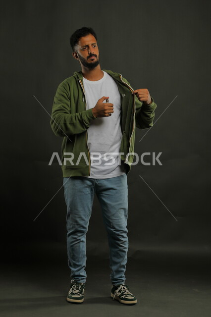 Marketing of perfume products, the concept of perfuming and perfuming, Saudi Gulf perfumes, attention to external appearance, the use of natural essential oils, a portrait of a young Saudi Gulf Arab man wearing a casual outfit spraying perfume, full-length body portrait, black background