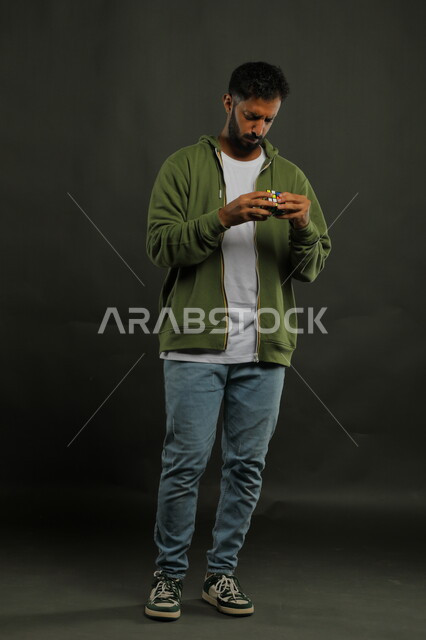 ألعاب تنمية الذكاء والمهارات العقليه، نشاطات تقوية الذاكره، بورتريه لشاب وسيم عربي خليجي سعودي يرتدي الزي الكاجوال يمسك بيده المكعب السحري، الوقوف باستقامة بإيماءات التركيز والاندماج، قضاء أوقات ممتعه في العطلة الصيفية، صوة الجسم بالطول الكامل، خلفية سوداء