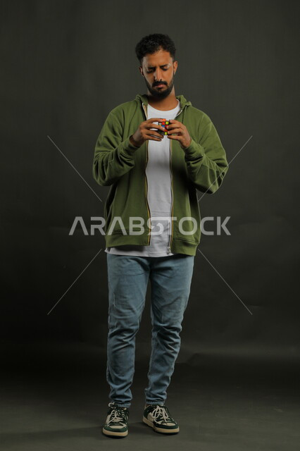 ألعاب تنمية الذكاء والمهارات العقليه، نشاطات تقوية الذاكره، بورتريه لشاب وسيم عربي خليجي سعودي يرتدي الزي الكاجوال يمسك بيده المكعب السحري، الوقوف باستقامة بإيماءات التركيز والاندماج، قضاء أوقات ممتعه في العطلة الصيفية، صوة الجسم بالطول الكامل، خلفية سوداء