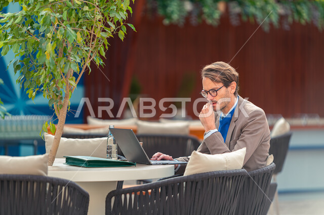 تحقيق رؤية السعودية ٢٠٣٠، ريادة في تعزيز الفرص الاقتصادية العالمية في مدينة الرياض، رجل أعمال من رواد مبادرة مستقبل الاستثمار يجلس على الطاولة ويسخدم اللابتوب في مركز الملك عبد العزيز للمؤتمرات، دافوس في الصحراء، دور المملكة في النمو الاقتصادي والنهضة التنموية.