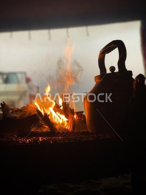 Enjoying hot drinks in winter, a close-up of a teapot on a burning wood fire, good generosity and hospitality, the joy of drinking tea on road trips in the winter