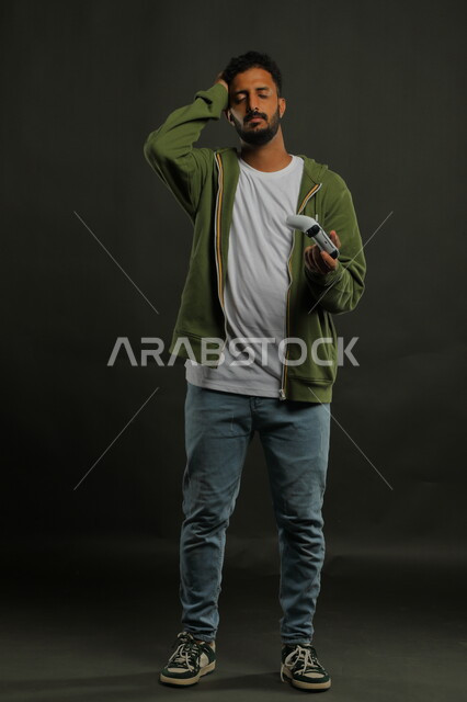 الالعاب الالكترونيه الترفيهية والممتعة، ايماءات الخسارة والحزن، بورتريه لشاب عربي سعودي خليجي يرتدي الزي الكاجوال يمسك يد التحكم ويضع يده على رأسه بحسرة، المتعة والتسلية بالفيديو جيمز،  صورة الجسم بالطول الكامل، خلفية رمادية