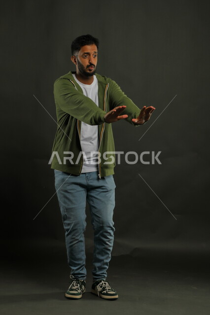 حماية النفس من ضرر خارجي, طلب الابتعاد وعدم الاقتراب,  رفع اليدين بإيماءات الاحتياط والقلق والتوقف , بورتريه لرجل عربي خليجي سعودي يرتدي الزي الكاجوال و يقف بحذر, صورة الجسم بالطول الكامل, خلفية سوداء